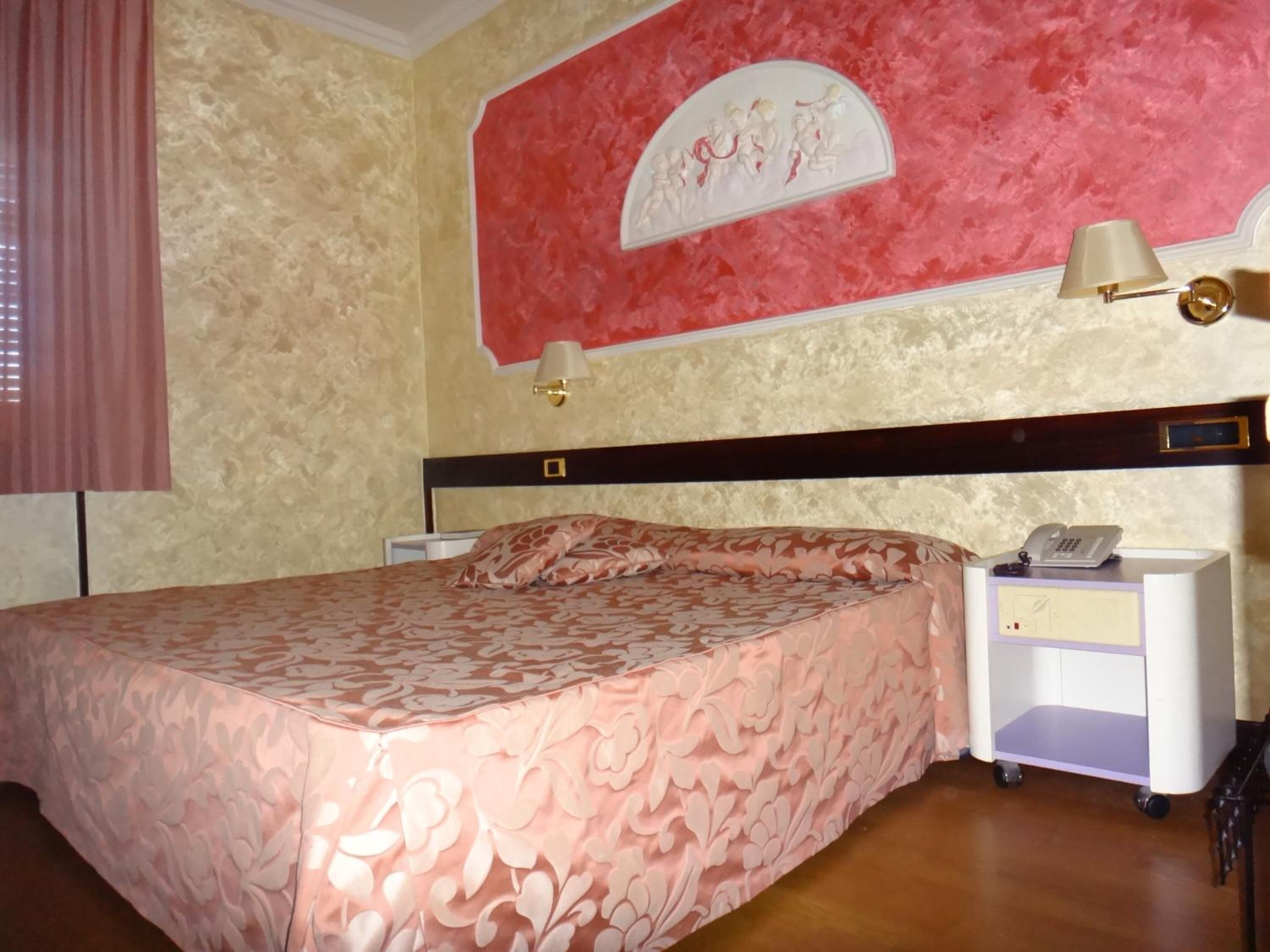 Ein Hotelzimmer mit einem Bett, einem Nachttisch mit Lampe, einem Telefon und einem kleinen Schrank.