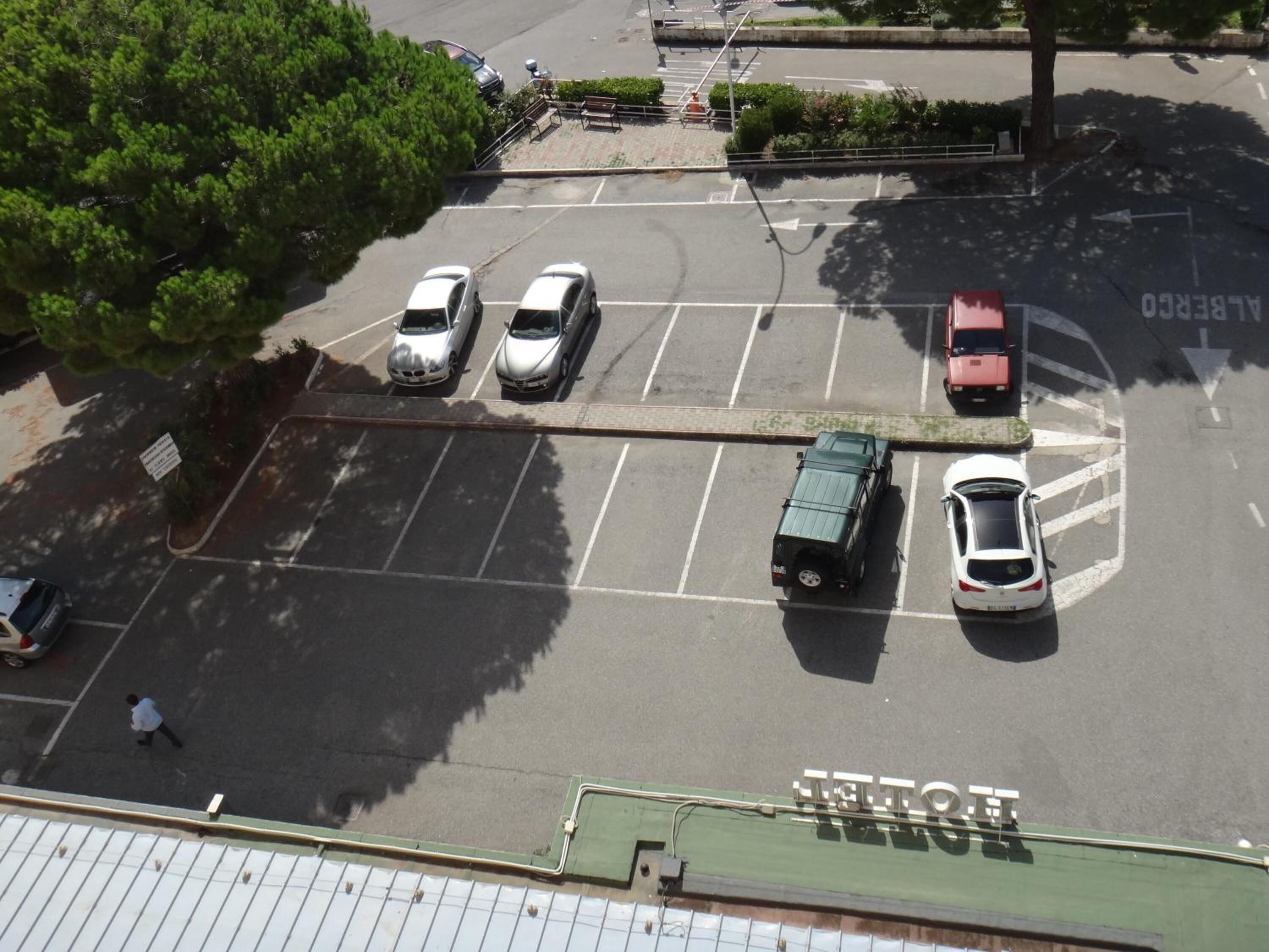 An aerial view of a parking lot with multiple cars, a green truck, and a pedestrian walking.