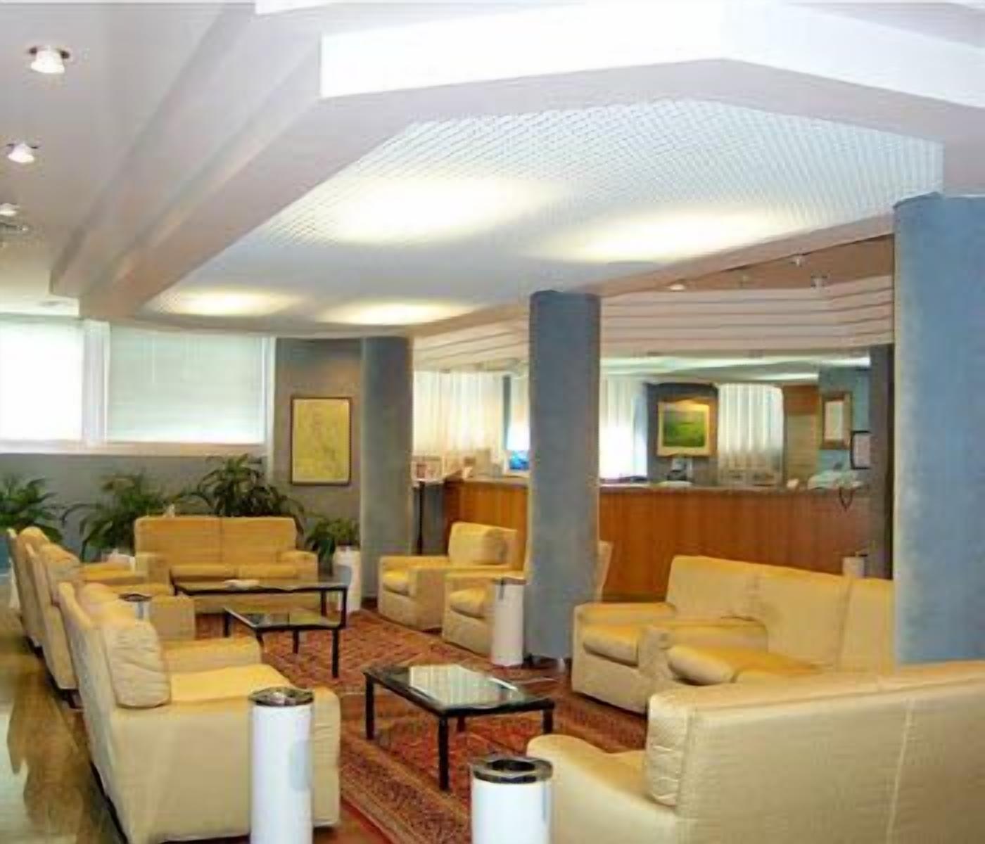 A spacious lobby with multiple seating areas, a reception desk, and a large window providing natural light.