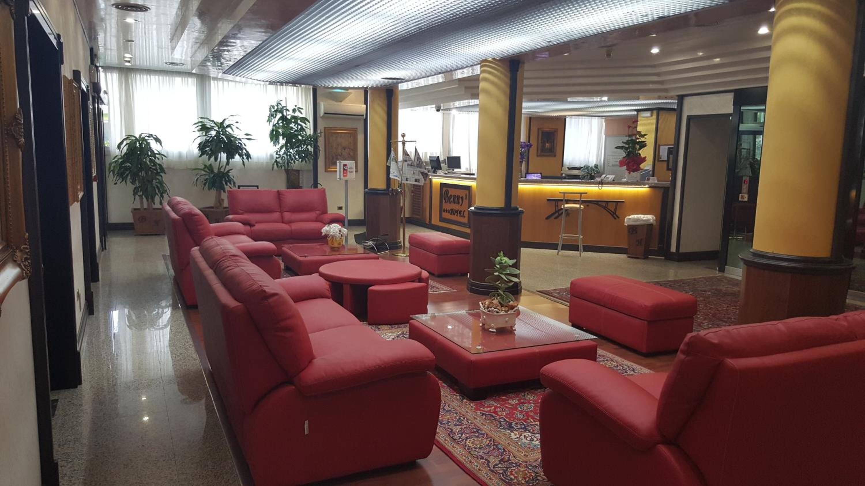 Una hall con sedute rosse, una reception e piante in vaso.