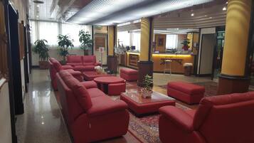 A lobby with red seating, a reception desk, and potted plants.