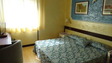 Ein Hotelzimmer mit Bett, Schreibtisch, Stuhl, Nachttisch und Lampe.