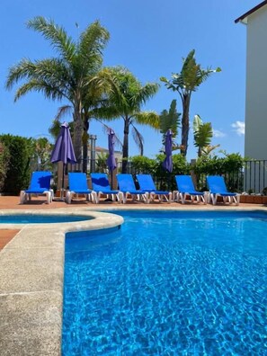 A swimming pool with blue water, surrounded by lounge chairs and palm trees.