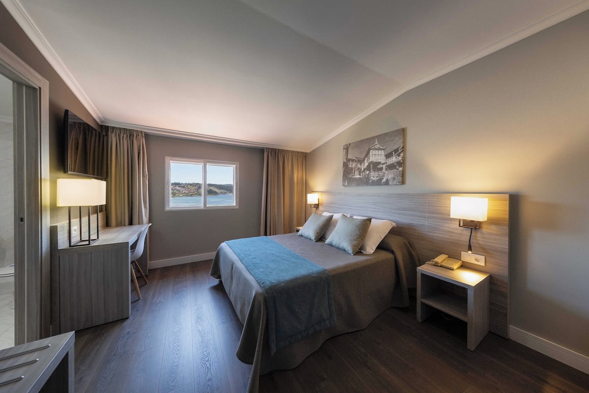 A hotel room with a large bed, bedside tables, a desk, and a window with a view.