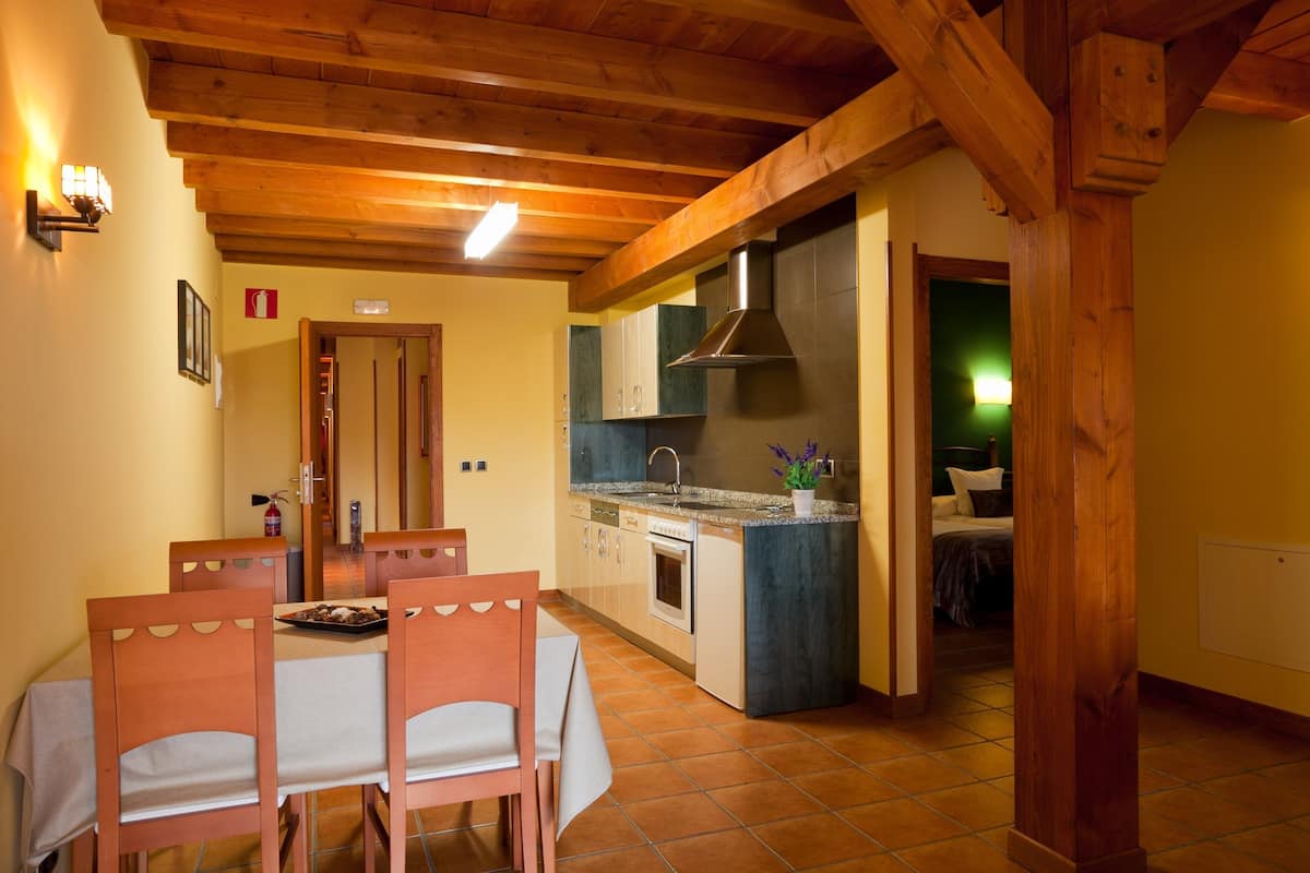 A compact kitchen with wooden beams, a dining area with a table and chairs, and a visible door leading to another room.