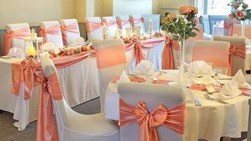 Un salón de banquetes con mesas dispuestas para un evento formal, decorado con centros de mesa florales y velas.