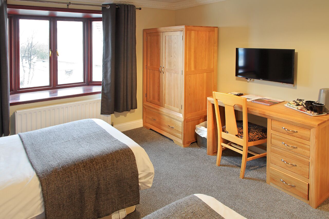 A hotel room with a bed, a desk with a chair, a wardrobe, a television, and a window with curtains.