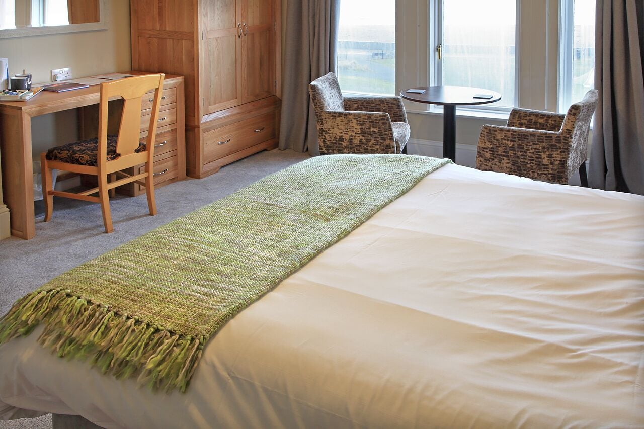 A hotel room with a large bed, a desk with a chair, a wardrobe, and a view of the city through the window.