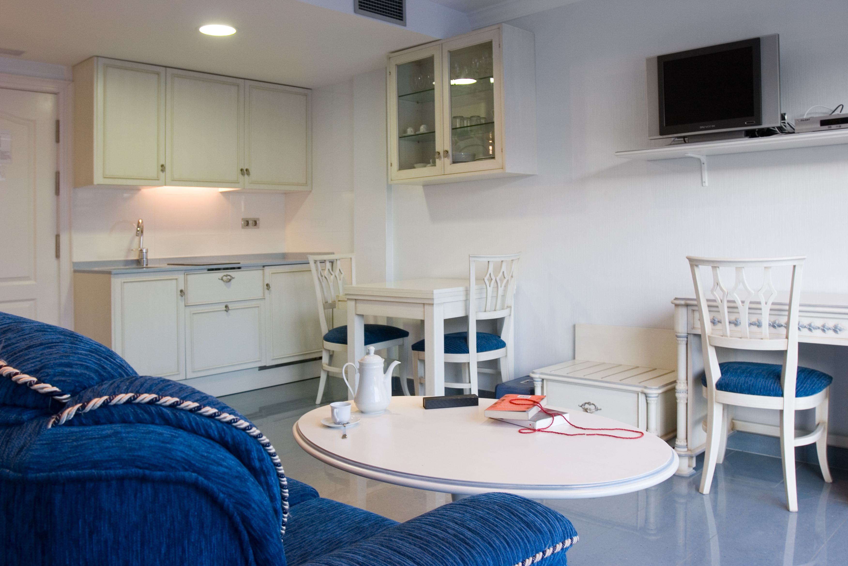 Un espacio habitable compacto con kitchenette, una zona de comedor con una mesa redonda y sillas, y un sofá.