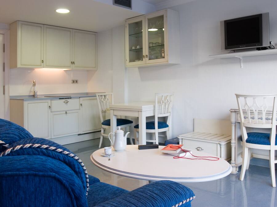 Un espacio habitable compacto con kitchenette, una zona de comedor con una mesa redonda y sillas, y un sofá.