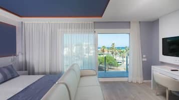 A modern hotel room with a bed, a sofa, a TV, and a balcony with a view of the city and palm trees.