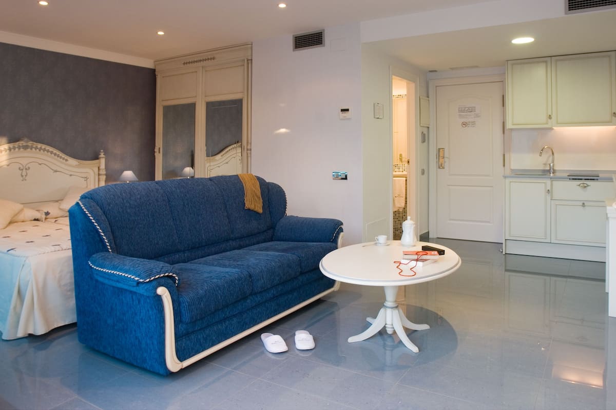 A room with a blue sofa, a small round table, and a bed with a white headboard.