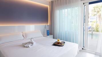 A modern hotel room with a large bed, a tray with breakfast, a swan-shaped towel, and a view of the outdoors through a sliding door.