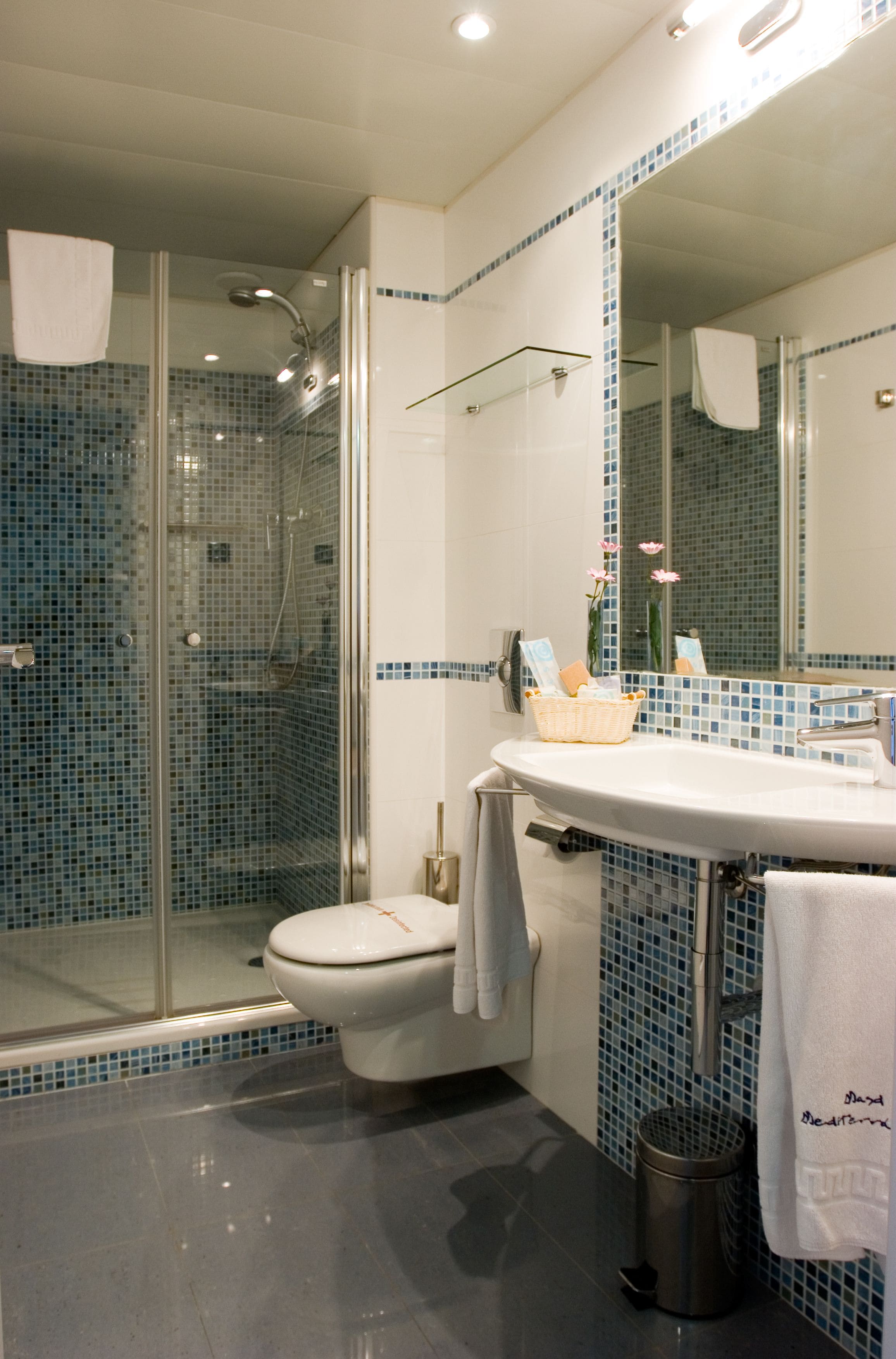 A bathroom with a glass-enclosed shower, a white sink, and a mirror with a blue-tiled backsplash.