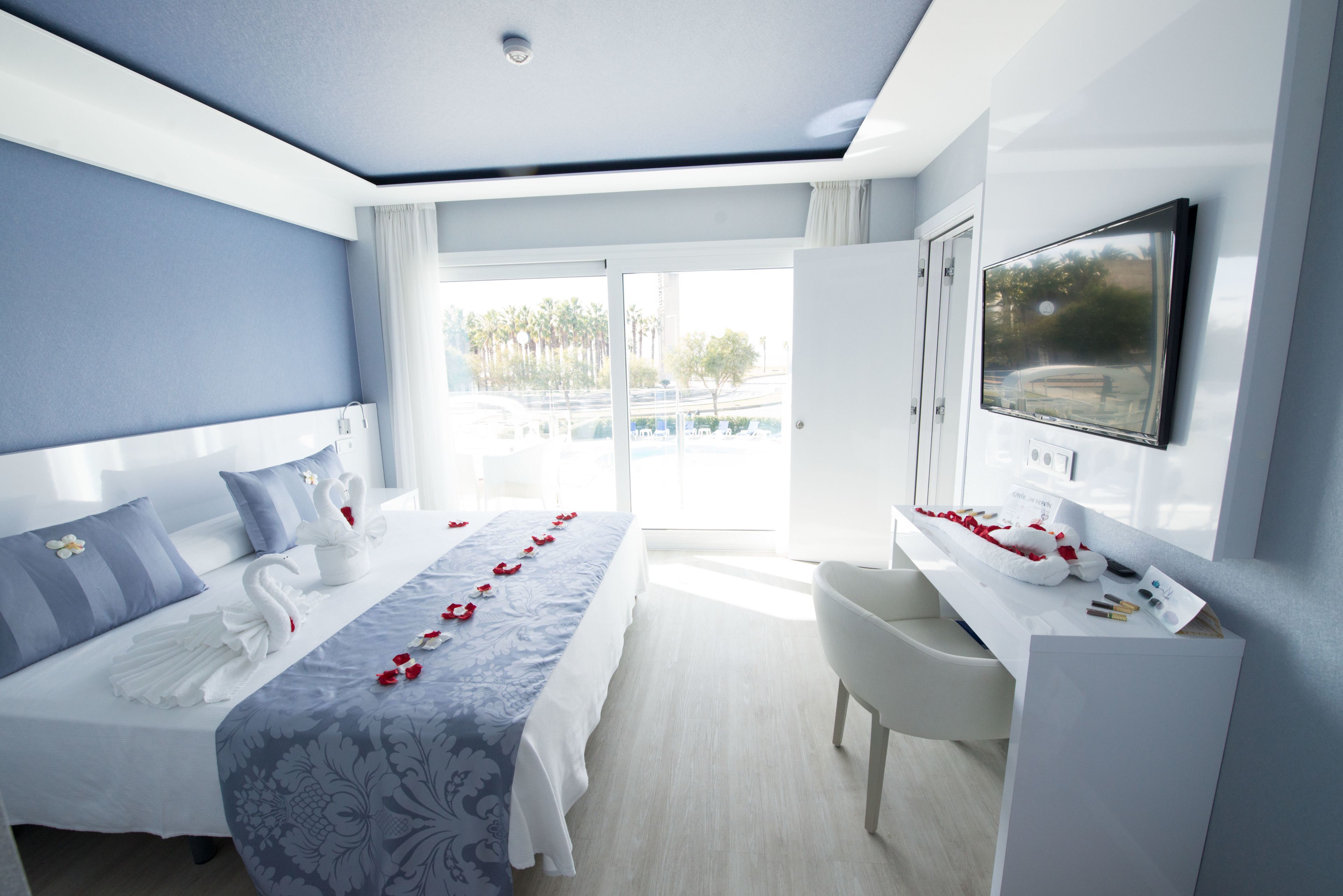 A modern hotel room with a large bed, a desk, a TV, and a view of the outdoors.