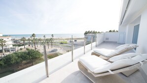 Un balcón con vista a la playa, sillas de descanso y un edificio moderno.