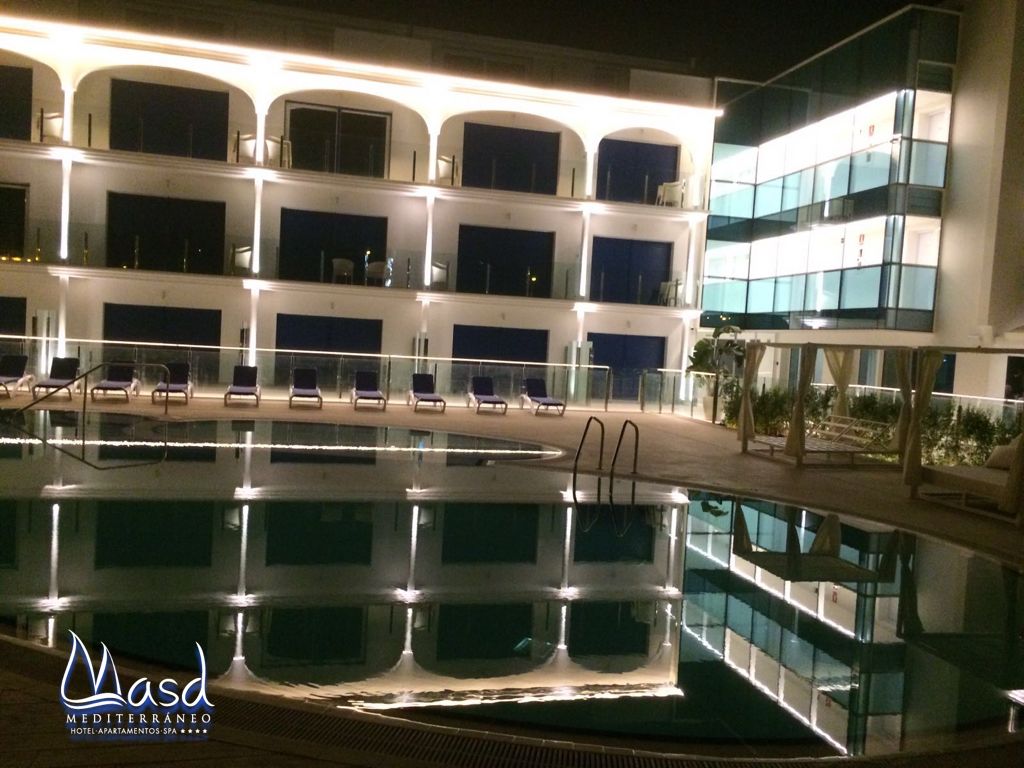 A swimming pool with lounge chairs and a building with multiple balconies in the background.