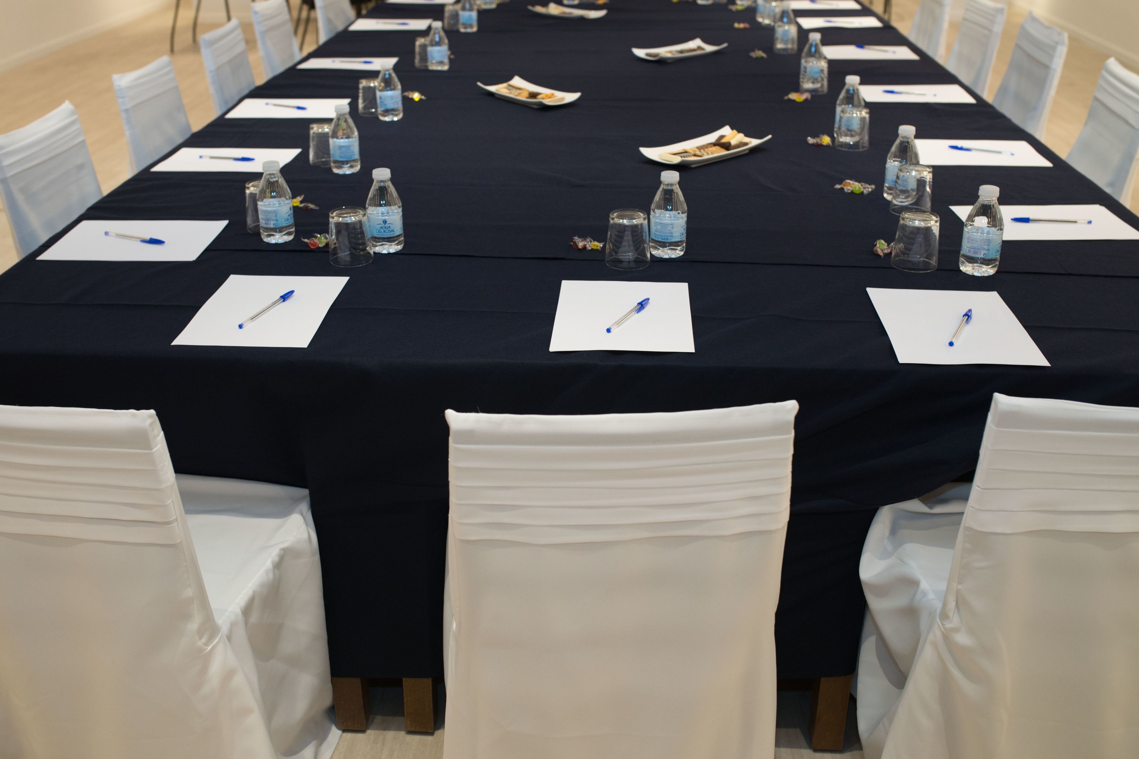 Una mesa de conferencias dispuesta con botellas de agua, bolígrafos y blocs de notas.