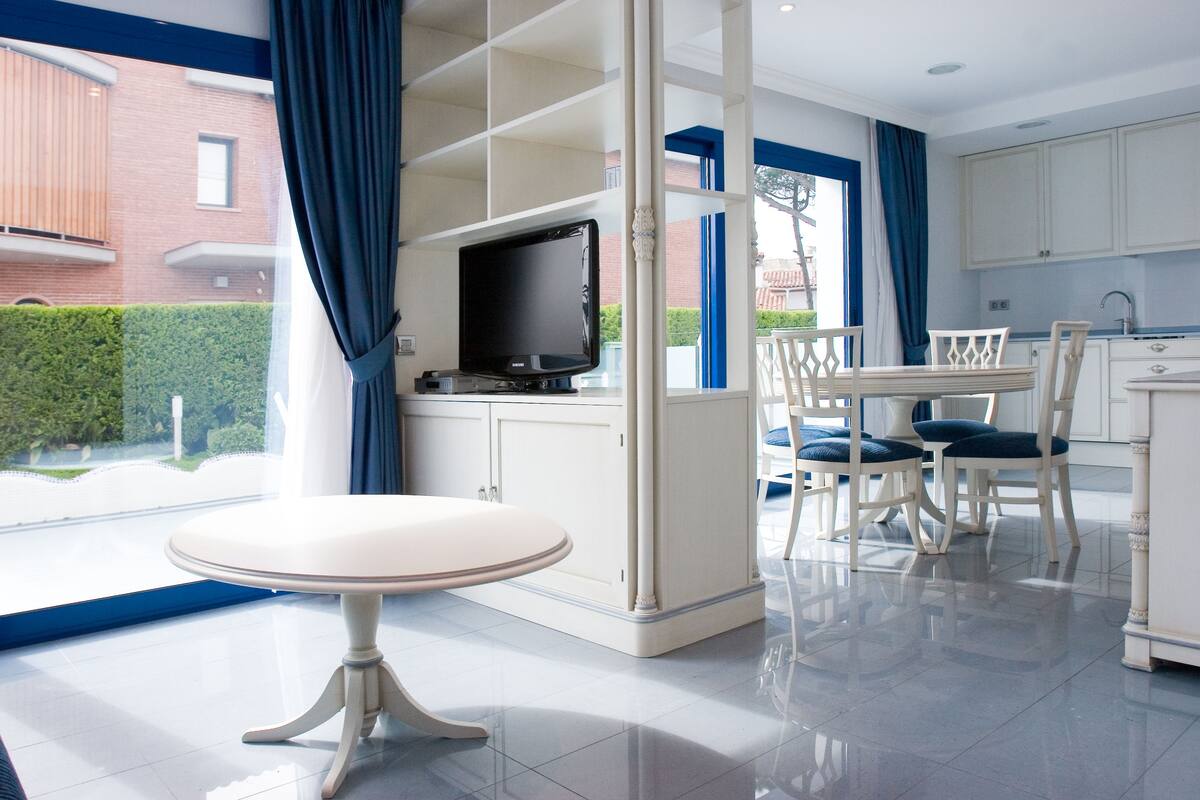 A modern kitchen with white cabinets, a dining table with chairs, and a television on a stand.