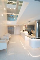 Un moderno vestíbulo de hotel con mostrador de recepción, zona de estar, ascensores y techo de cristal.