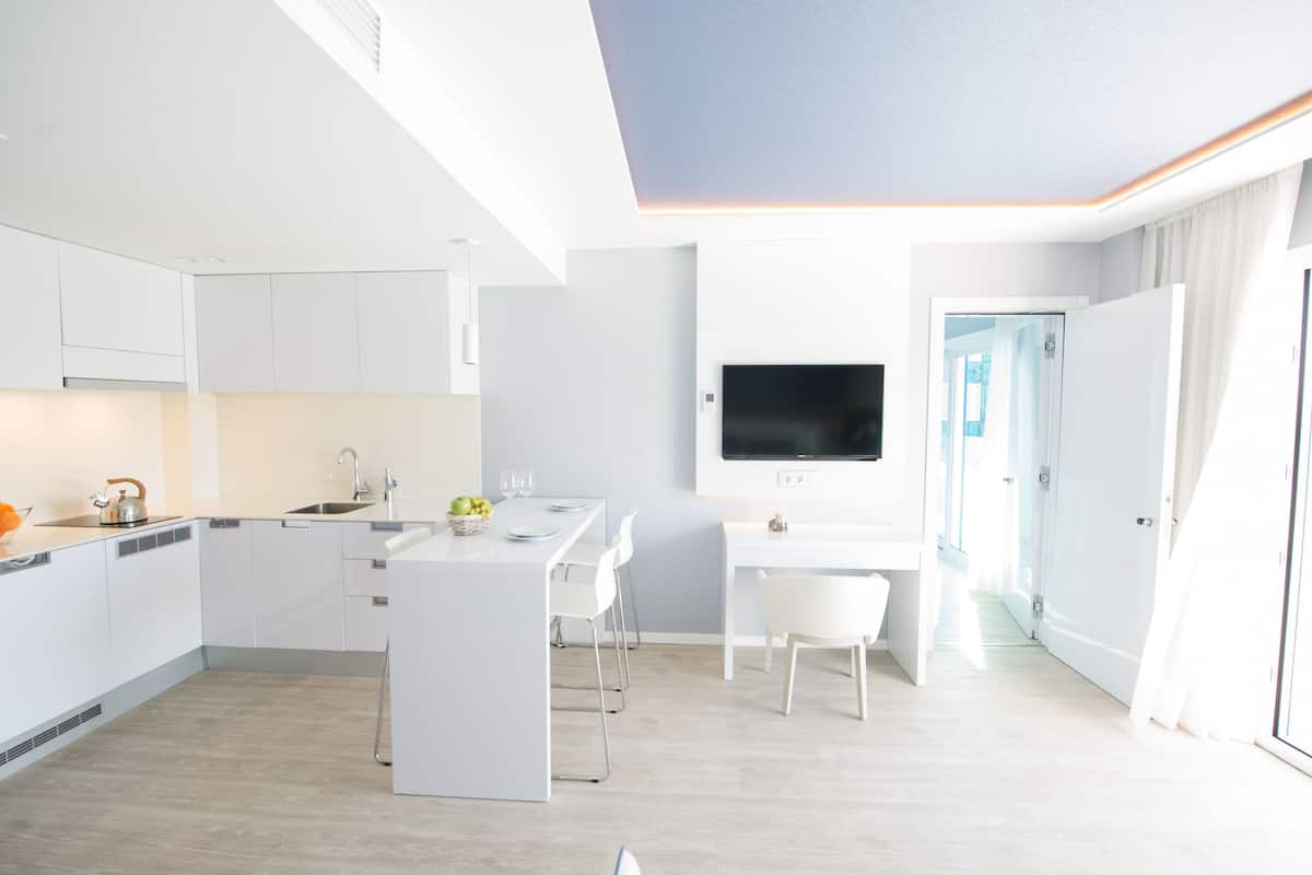 A modern kitchen with white cabinetry, a central island, and a dining area with white chairs.