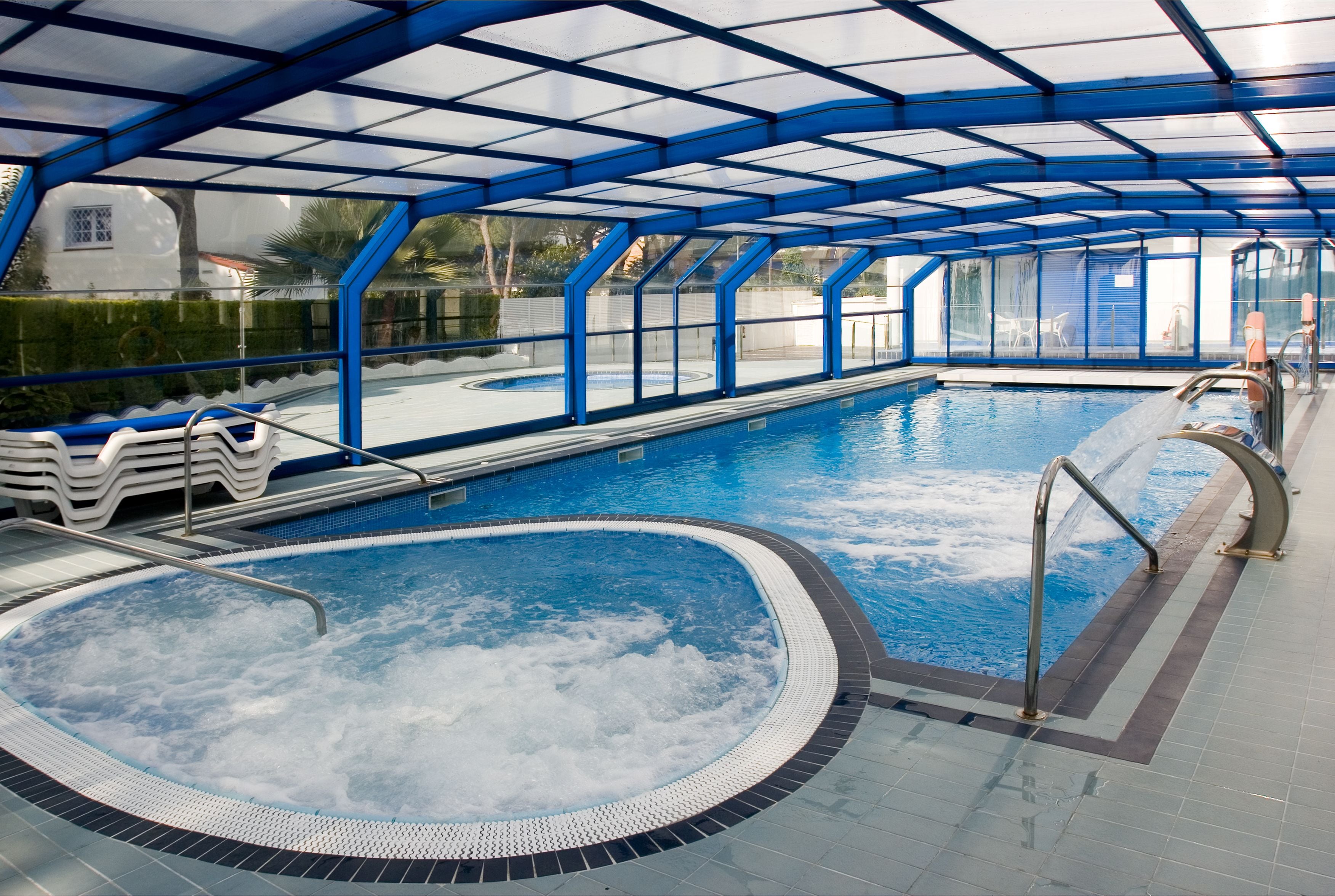 Una piscina techada con un jacuzzi, agua azul cristalina y un deck de cerámica.