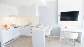 Een moderne keuken met witte kasten, een eethoek met een witte tafel en stoelen, en een tv aan de wand.