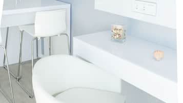 Habitación moderna y minimalista con un escritorio blanco, una silla blanca, un televisor montado en la pared y un pequeño adorno en el escritorio.