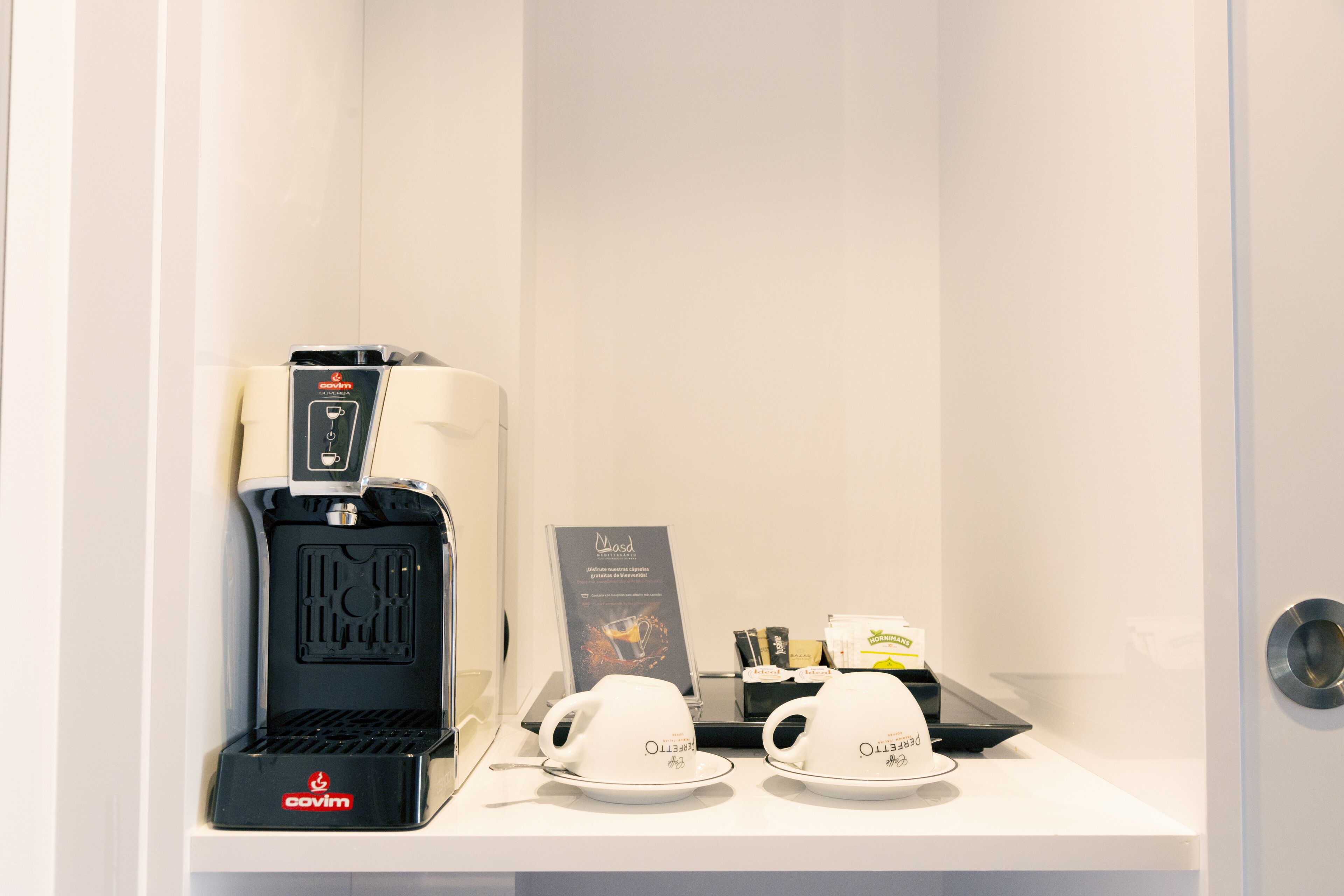 A coffee machine, two cups, and a sign in a hotel room.