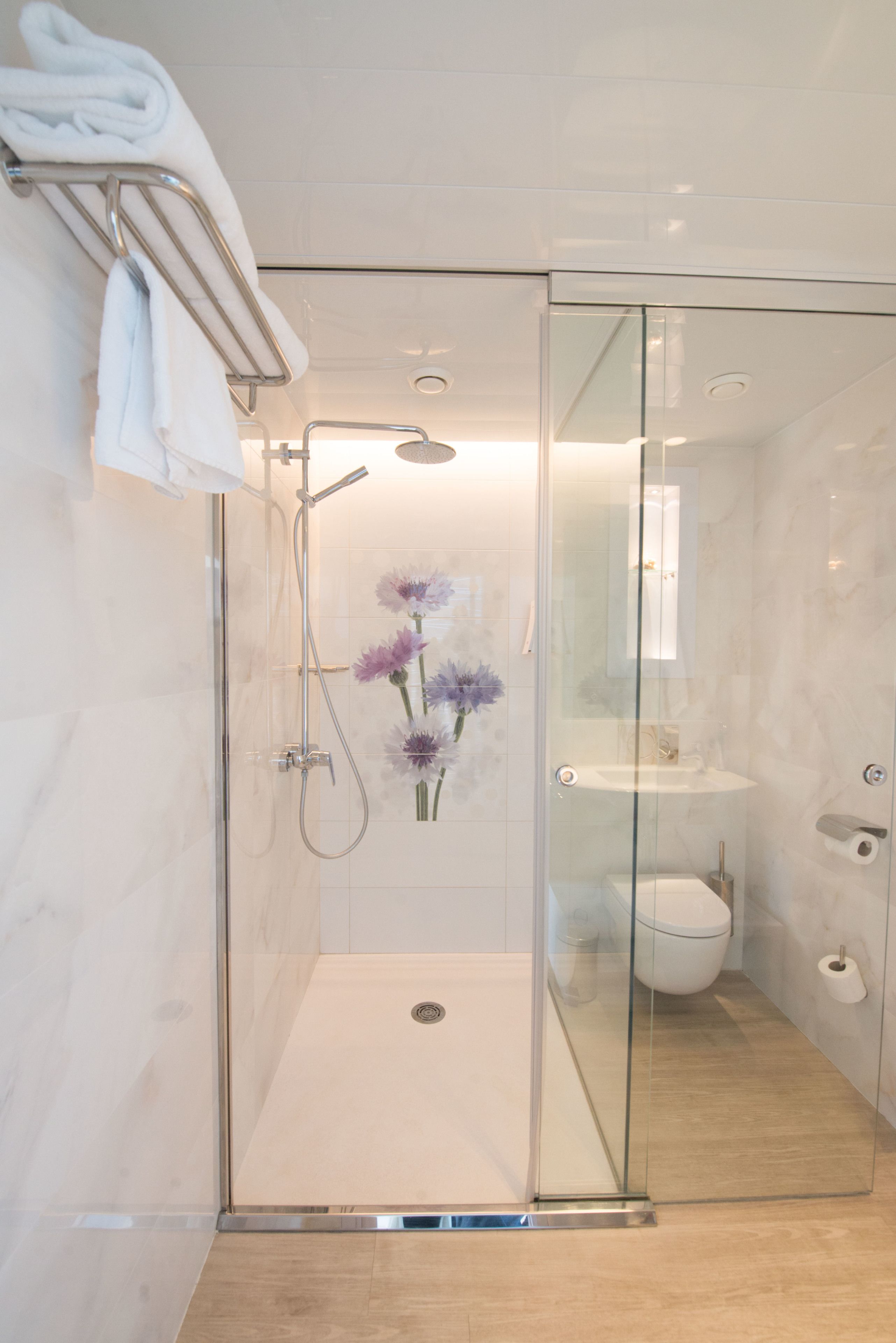 A modern shower with a glass door, a white towel on a metal rack, and a glass-enclosed toilet area with a marble floor.