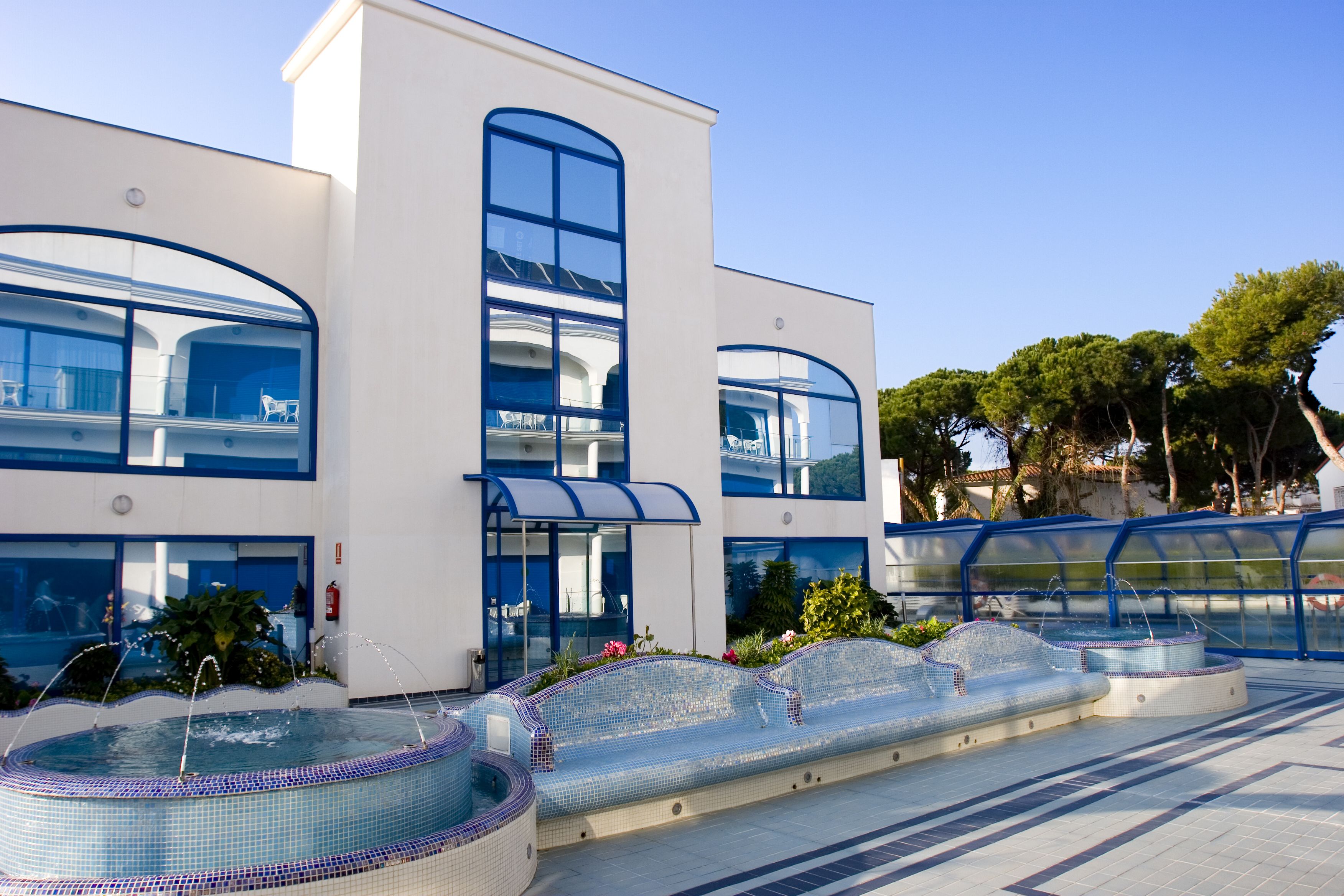 Un bâtiment moderne doté d’un espace piscine agrémenté de sièges recouverts de mosaïques et d’une enceinte en verre transparent.