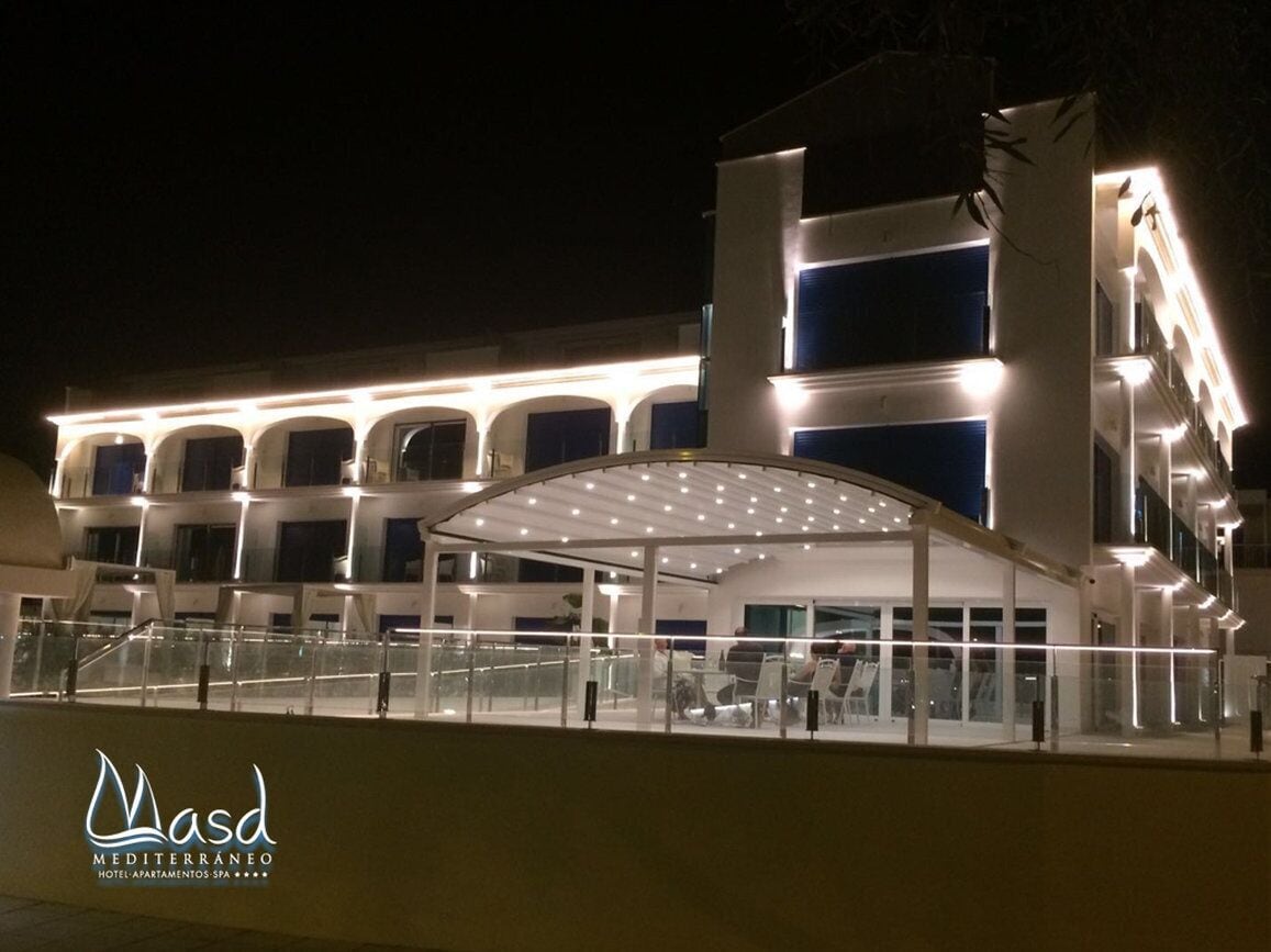 A hotel with a covered outdoor area, multiple balconies, and a well-lit facade at night.