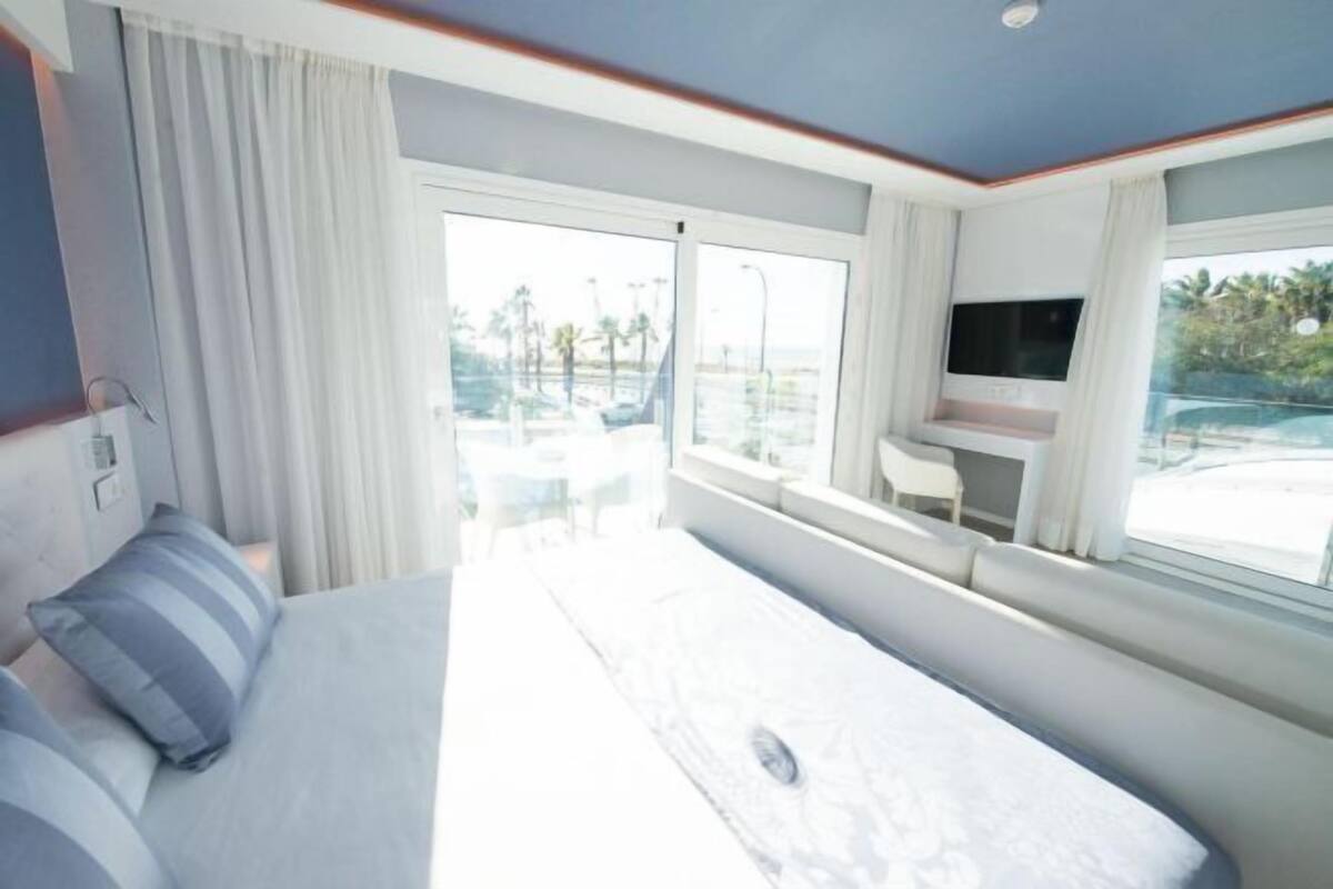 A hotel room with a bed, a TV, a desk, and a view of the outdoors.