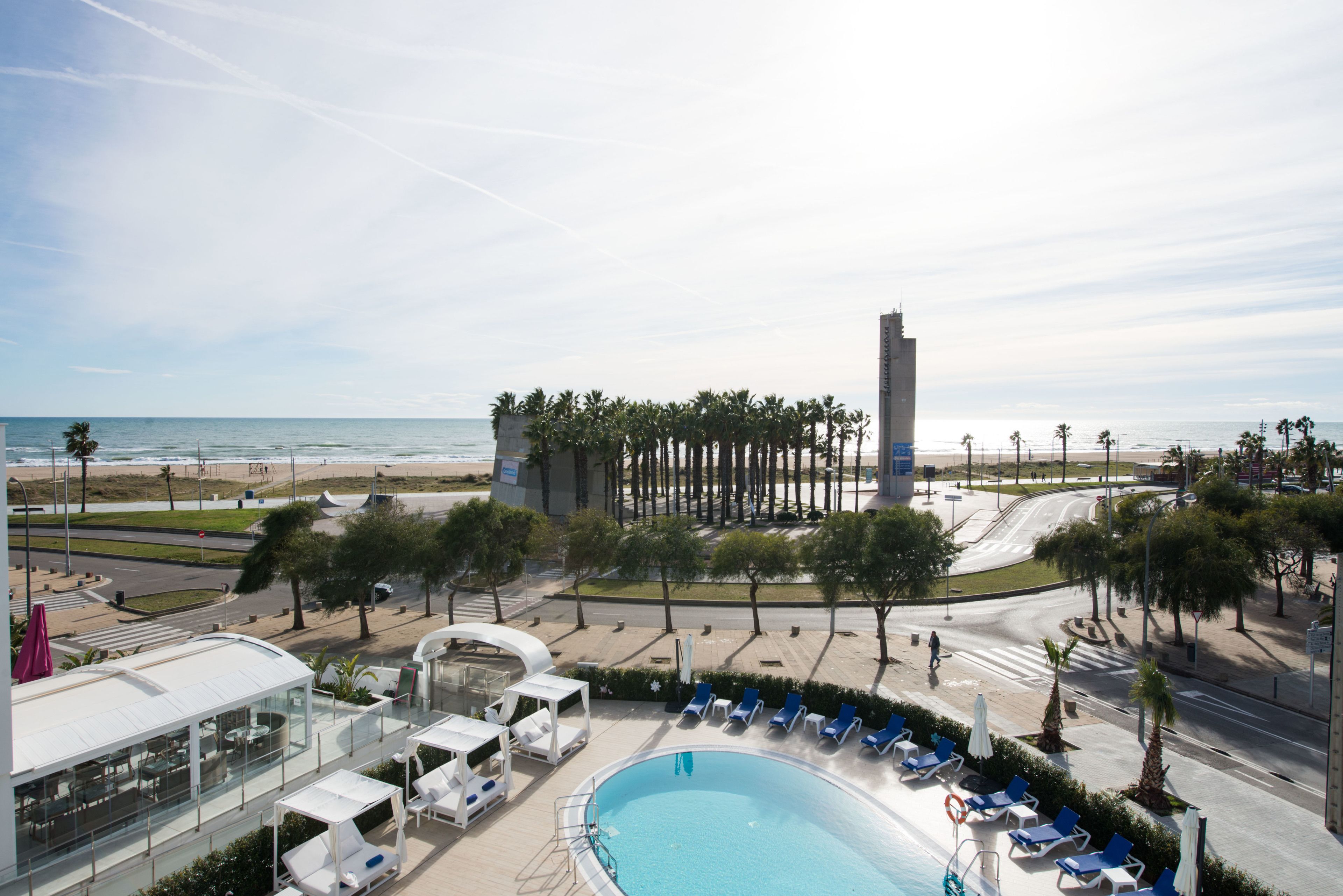 Un área de piscina en la azotea con sillones de descanso y un restaurante con cerramiento de vidrio.