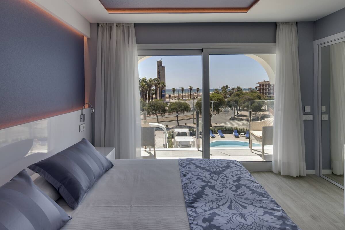 A modern hotel room with a large bed, a flat-screen TV, and a balcony with a pool view.