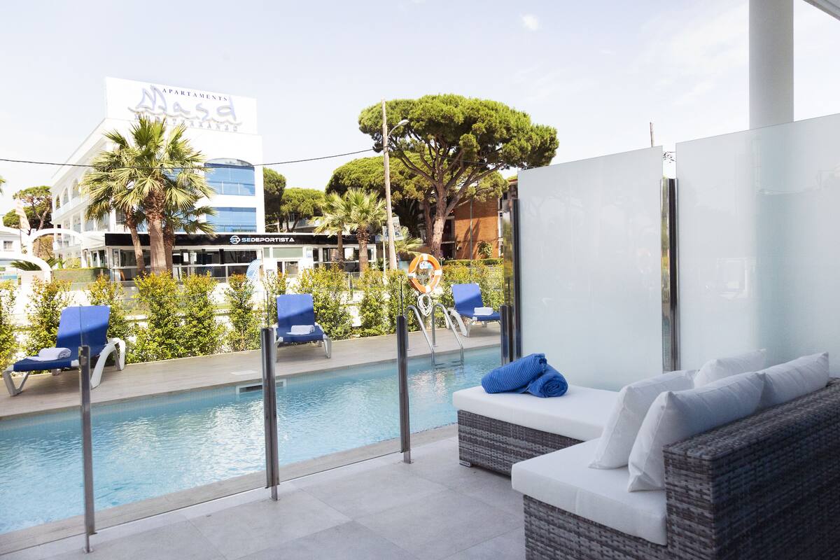 A poolside area with lounge chairs, a wicker sofa, and a view of a building with a sign.