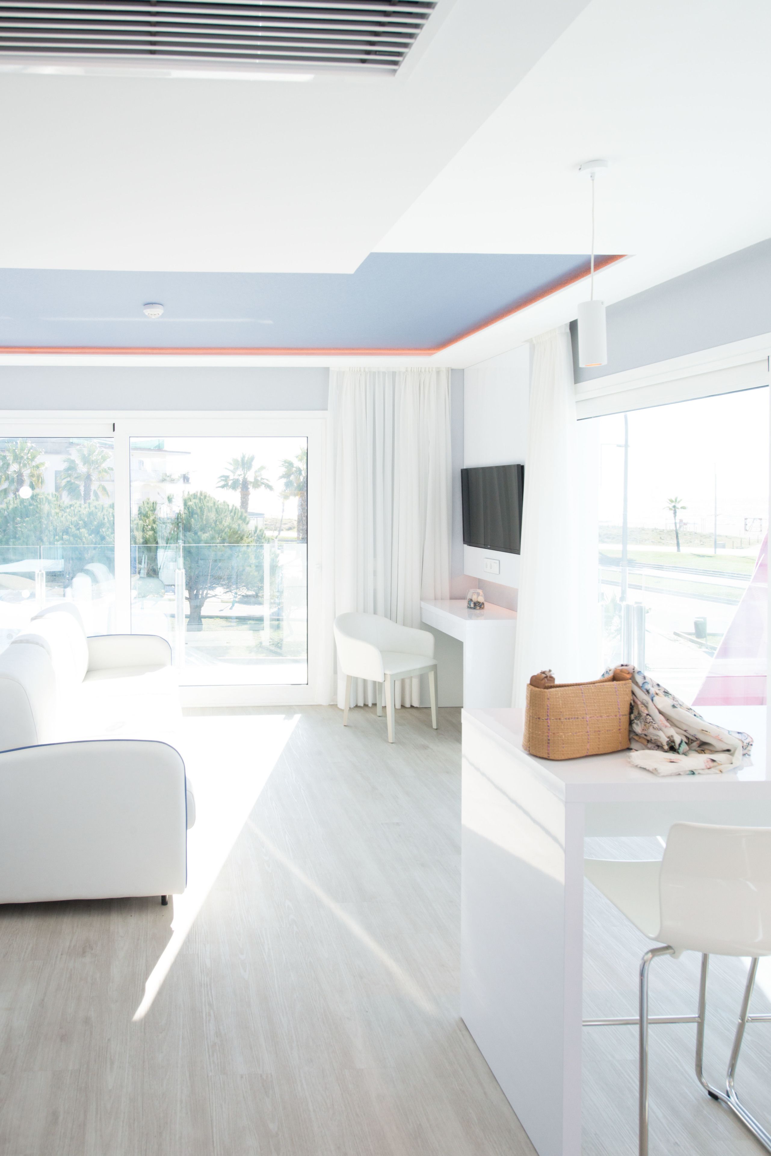 Een lichte, moderne hotelkamer met een ruim balkon, een flatscreen televisie, een wit bureau en een comfortabele zithoek.