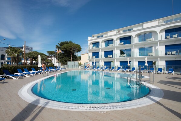 Zona de piscina con sillas reclinables azules y un edificio con varios balcones.