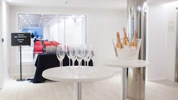 Un moderno vestíbulo de hotel con mostrador de recepción, un área de descanso con sillas rojas y una mesa con copas de champán y una cubeta de botellas de champán.