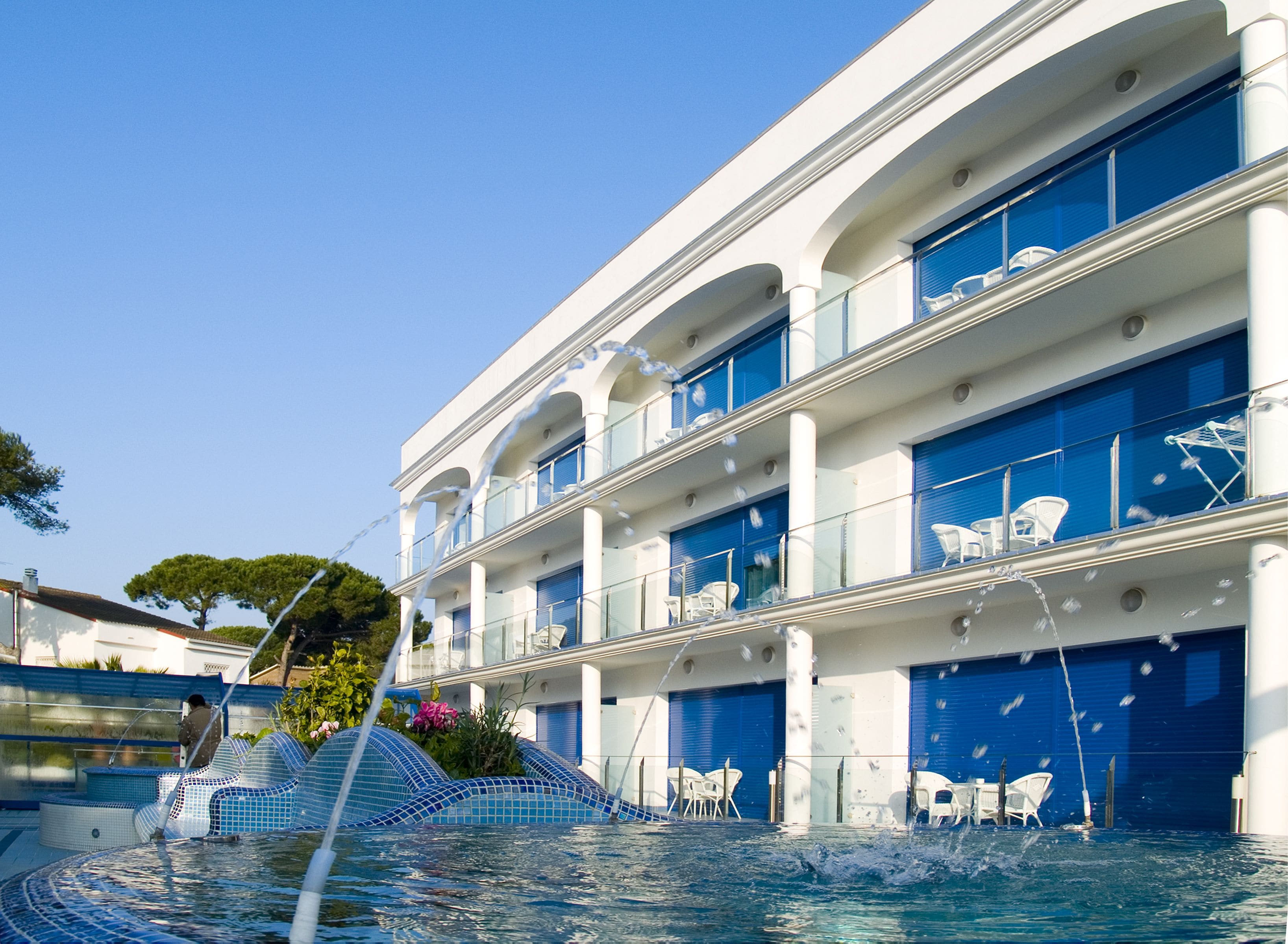 Un hotel de varios pisos con balcones, piscina y fuente de agua.