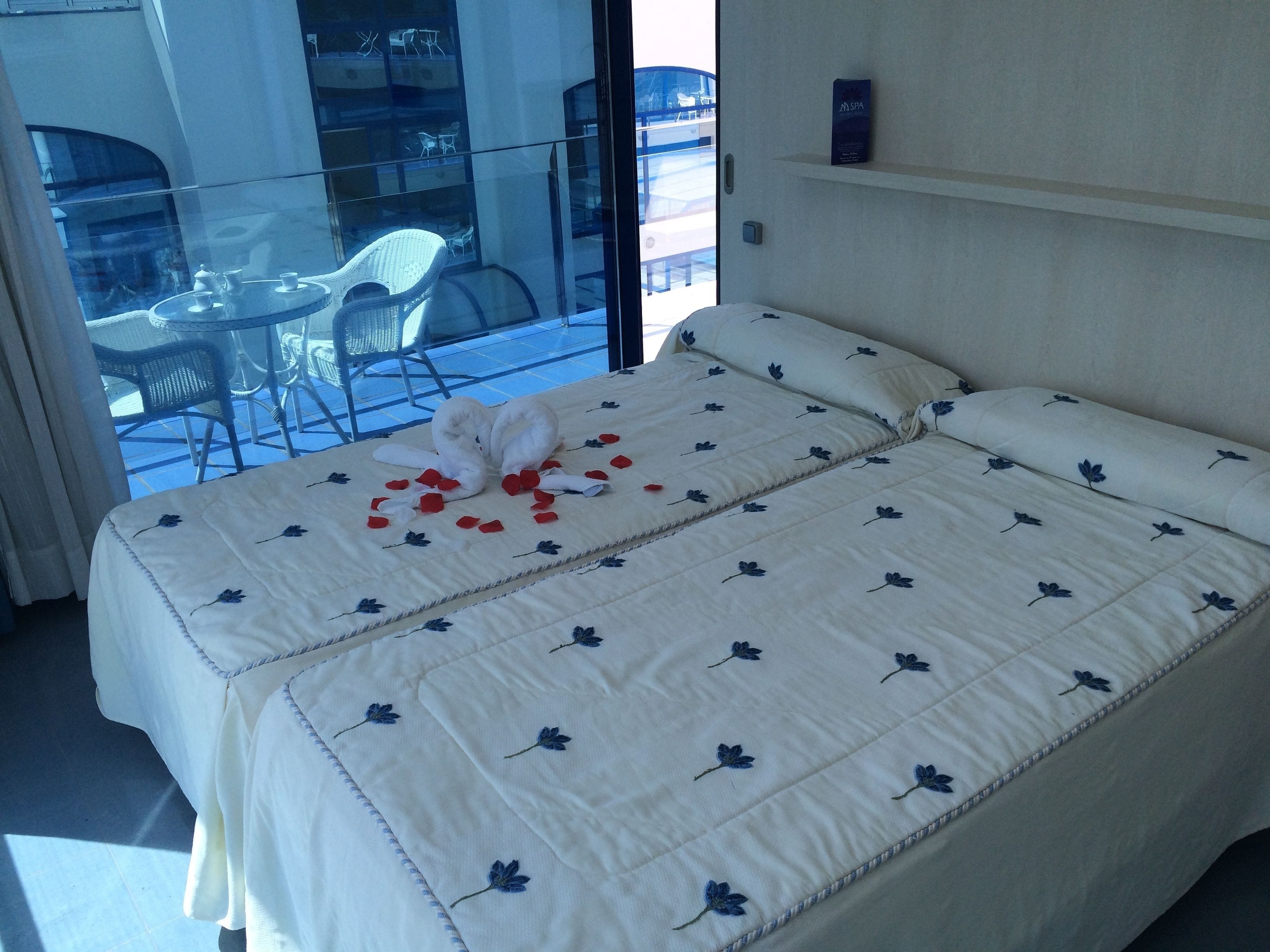 Une chambre d’hôtel avec un lit, une porte vitrée donnant sur un espace extérieur aménagé en salon, et un panneau indiquant la présence d’un spa sur le mur.