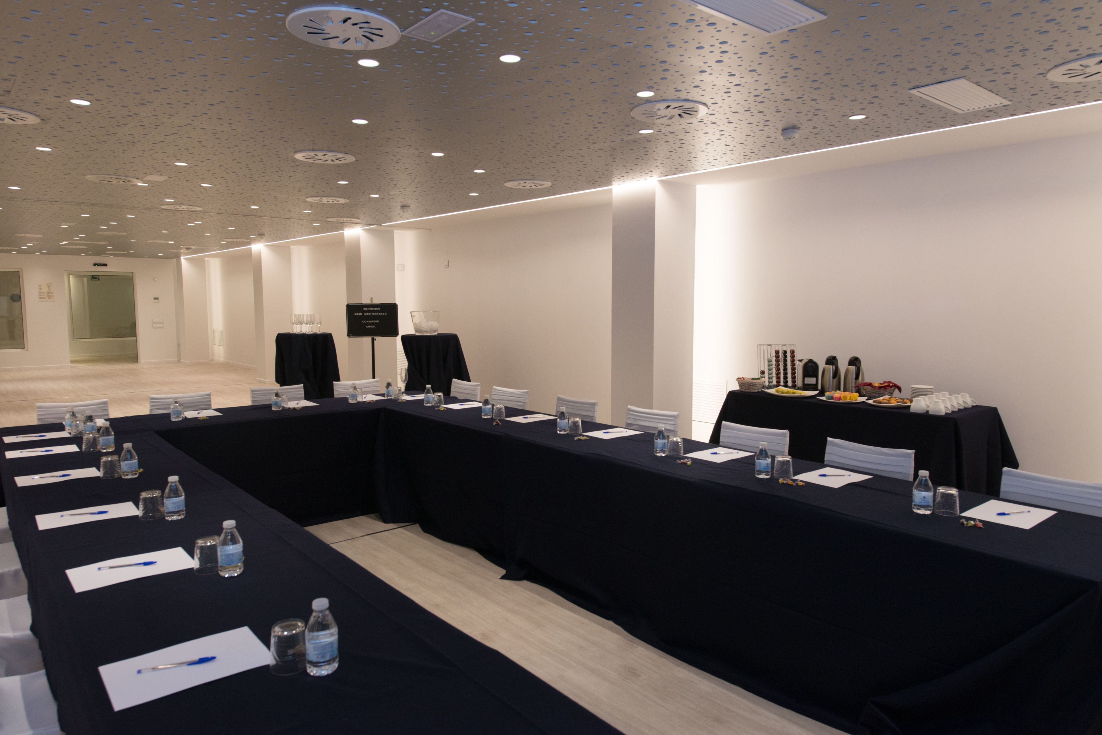 A conference room with a long table, nameplates, water bottles, and a buffet table with food and drinks.