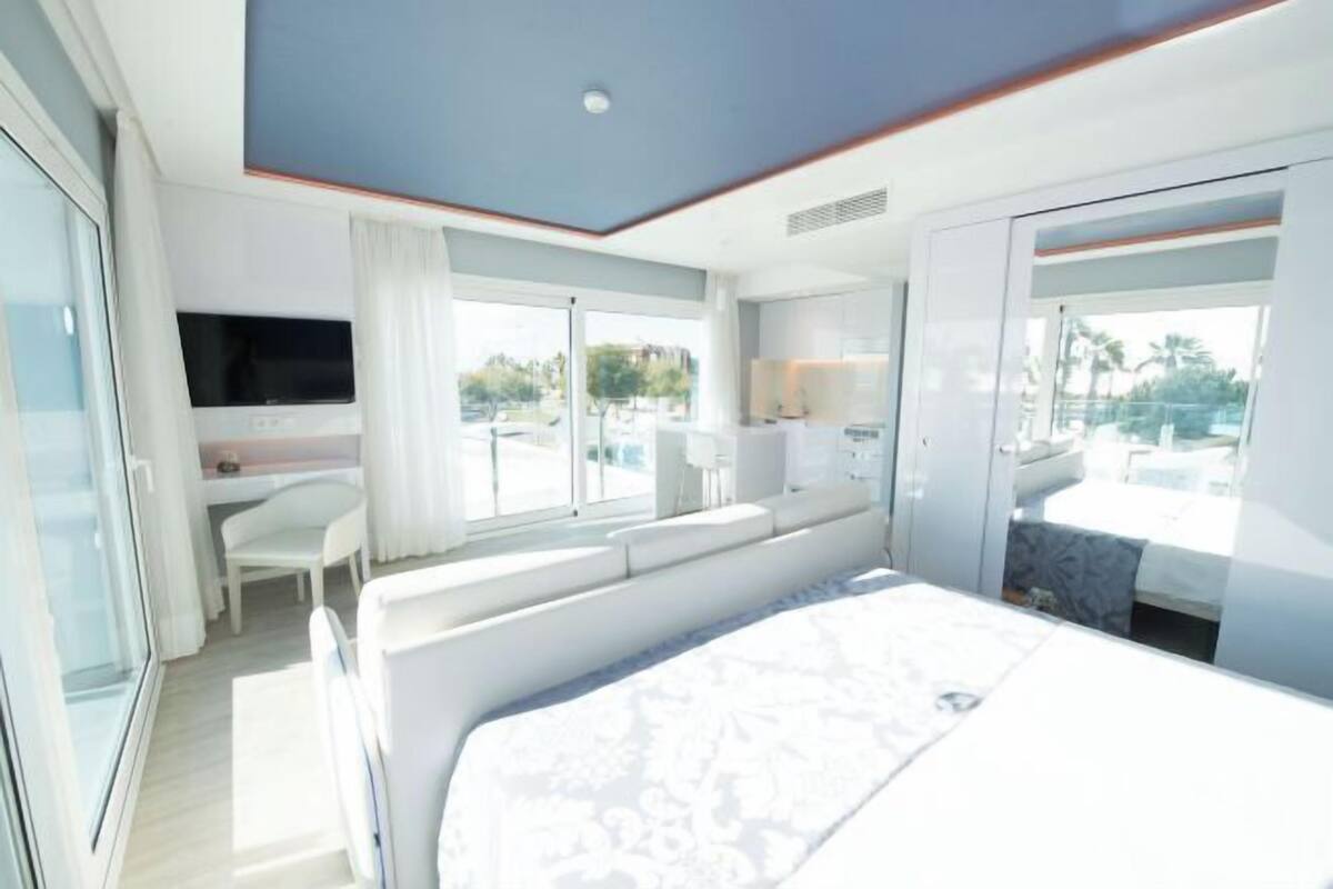 A modern hotel room with a large bed, a TV, a desk, and a balcony with a view.