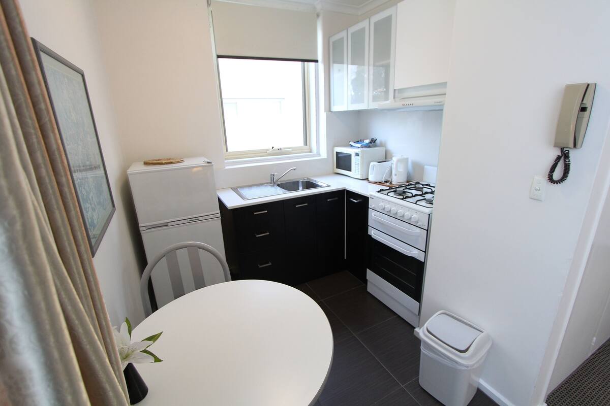 A compact kitchen with a sink, stove, microwave, and white cabinets.