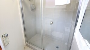 A glass-enclosed shower stall with a tiled floor and a door with a handle. - Drummond Apartments Services (Carlton)