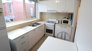 A compact kitchen with white cabinets, a gas stove, a microwave, and a sink. - Drummond Apartments Services (Carlton)