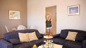 A living room with two sofas, a coffee table with a fruit bowl, and a three-tiered dessert stand. - Lavender House B&B (The Entrance)