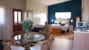 A hotel room with a bed, bedside table, lamp, TV, and a dining area with chairs and a table. - Lavender House B&B (The Entrance)