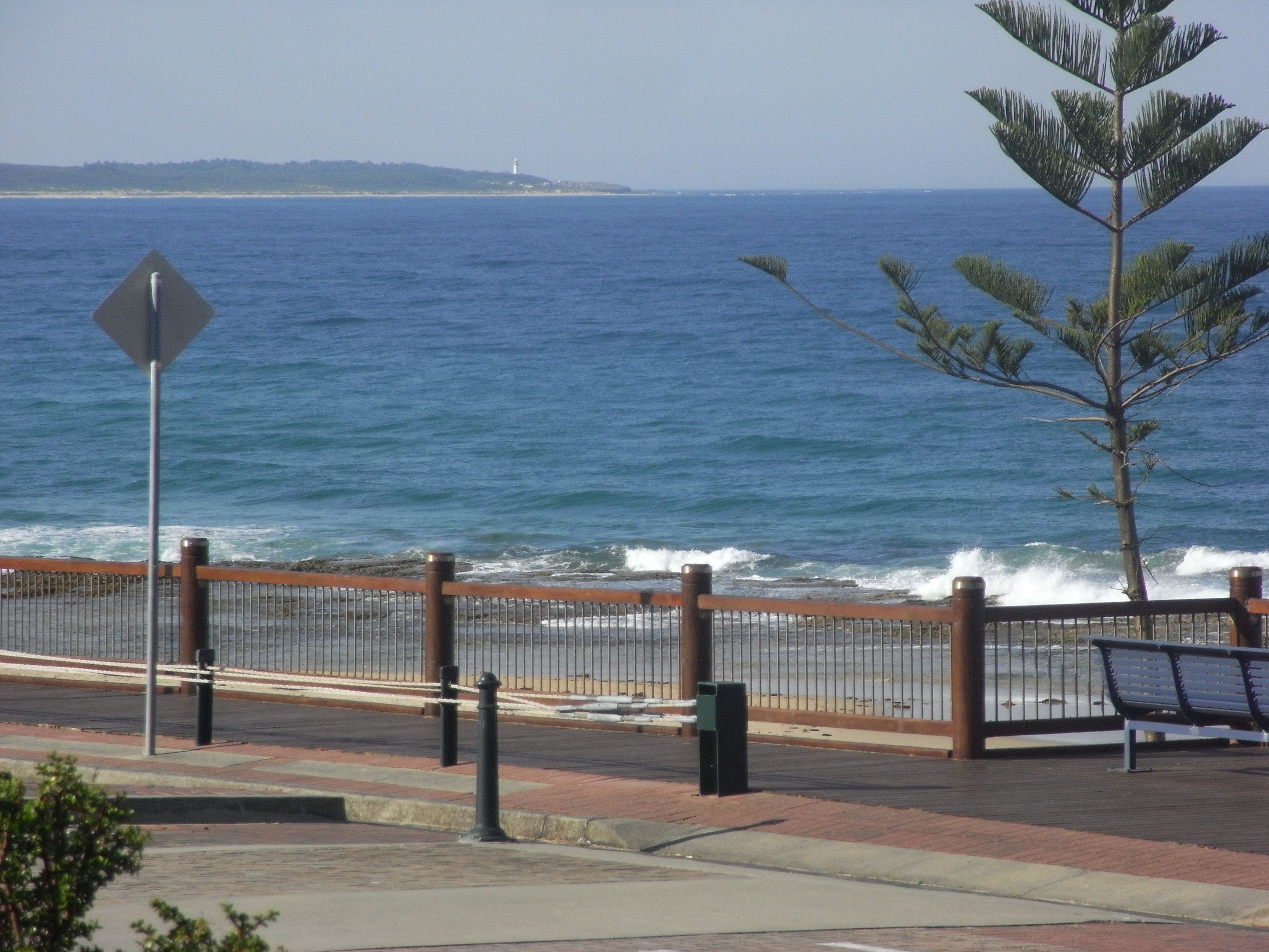 A coastal walkway with a metal fence, a bench, and a street sign.
