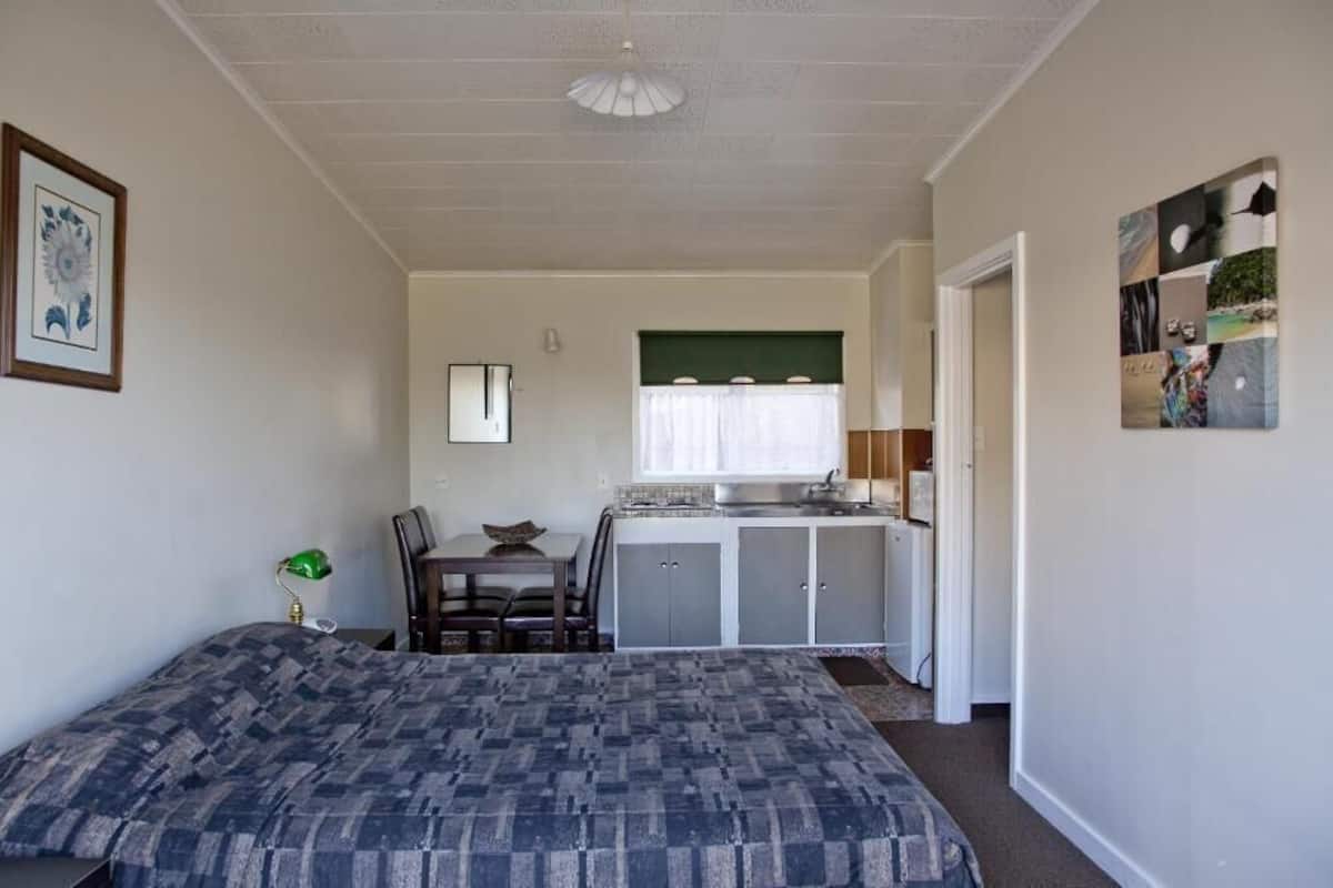 A compact room with a bed, a small dining table, a kitchenette, and a framed picture on the wall.